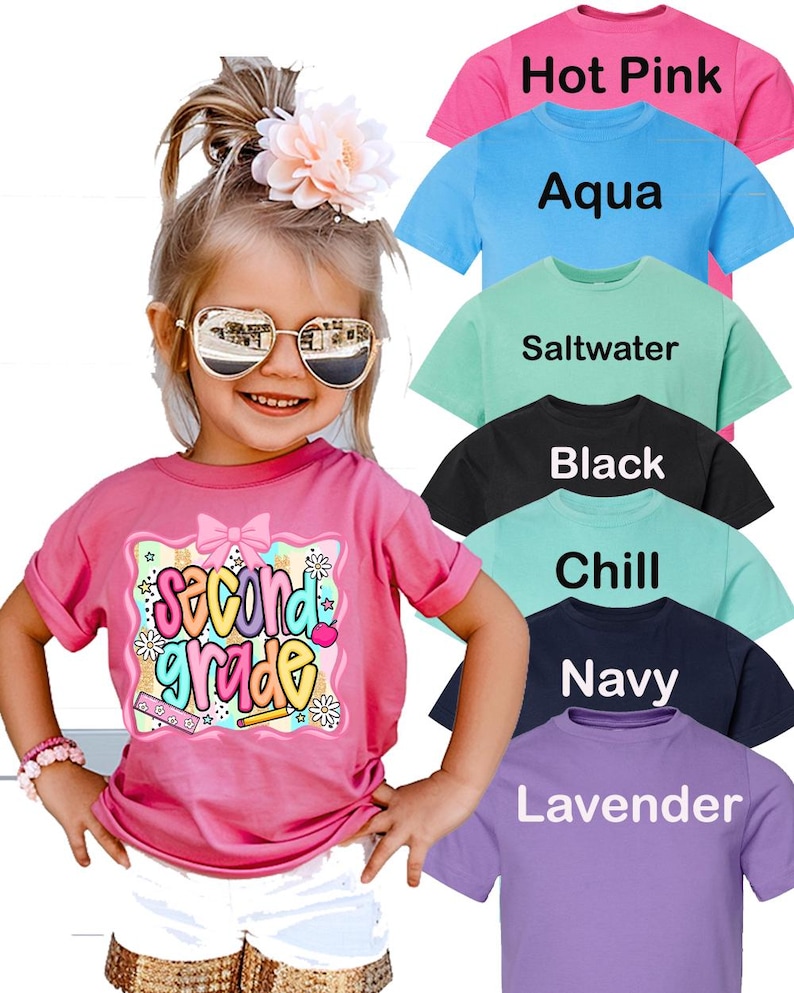 May include: A short-sleeved t-shirt in various colors including hot pink, aqua, saltwater, black, chill, navy, and lavender. The pink shirt features a graphic with the text "second grade," a bow, flowers, a ruler, and a pencil.