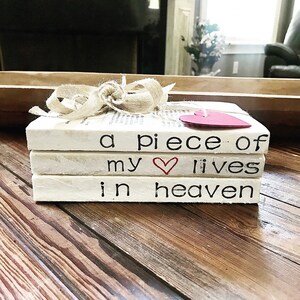 May include: A stack of three white books with a red heart and the text "a piece of my ♥ lives in heaven" on the top book. The books are tied with a brown ribbon.