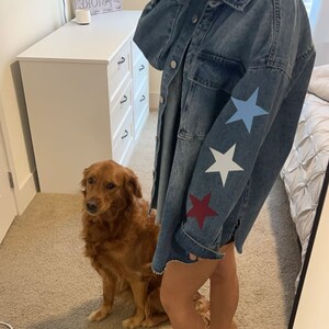 Peut inclure: Une veste en jean avec un ourlet effiloché et trois étoiles sur la manche. Les étoiles sont rouge, blanche et bleue. Un chien golden retriever est assis au premier plan.