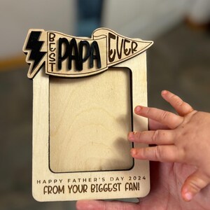May include: Wooden photo frame with a banner that says "Best Papa Ever" and a lightning bolt. The frame has a space for a photo and the text "Happy Father's Day 2024 From Your Biggest Fan!"