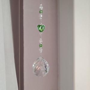 May include: A crystal suncatcher with a green heart charm and clear crystal beads hanging from a silver string.