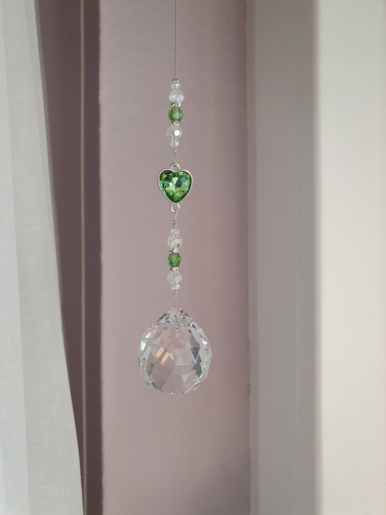 May include: A crystal suncatcher with a green heart charm and clear crystal beads hanging from a silver string.