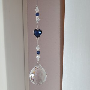 May include: A crystal suncatcher with a blue heart charm and clear crystal beads hanging from a silver string.