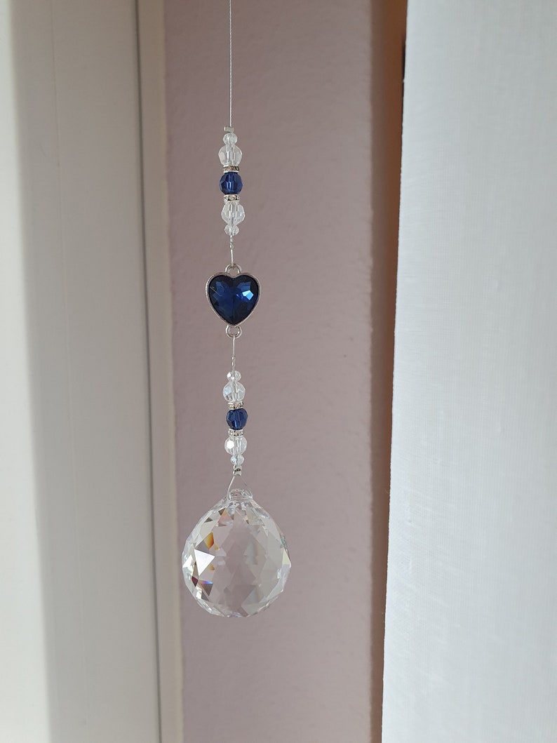 May include: A crystal suncatcher with a blue heart charm and clear crystal beads hanging from a silver string.