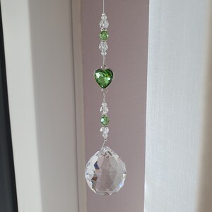 May include: A crystal suncatcher with a green heart charm and clear crystal beads hanging from a white string.
