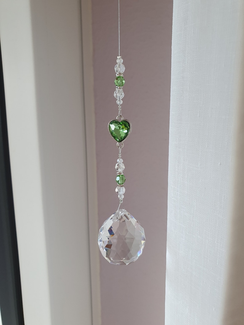 May include: A crystal suncatcher with a green heart charm and clear crystal beads hanging from a white string.
