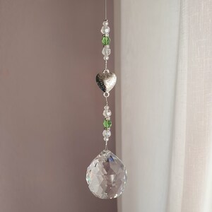 May include: A crystal suncatcher with a silver heart charm and green and clear beads hanging from a white string.