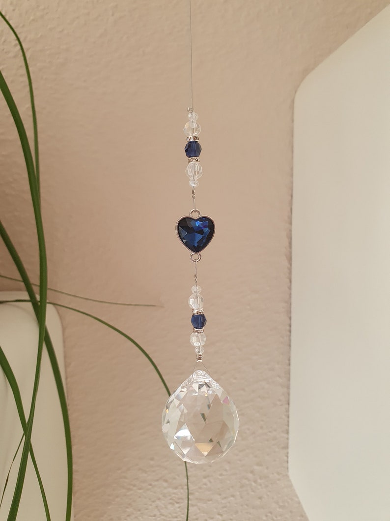 May include: A crystal suncatcher with a blue heart charm and clear crystal beads hanging from a silver string.