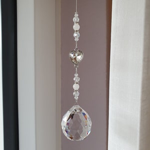 May include: A crystal suncatcher with a clear crystal ball and a silver heart charm hanging from a silver chain with white beads.