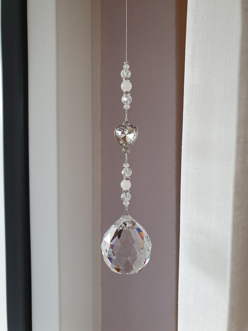 May include: A crystal suncatcher with a clear crystal ball and a silver heart charm hanging from a silver chain with white beads.