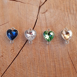 May include: Four heart-shaped charms with crystal accents in blue, clear, green, and gold. Each charm has a silver metal loop on the top and bottom.