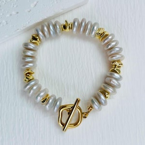 May include: A white pearl bracelet with a gold toggle clasp. The pearls are arranged in a staggered pattern and the clasp is a simple, rectangular design.