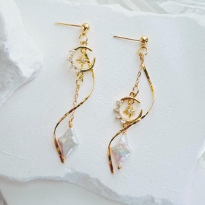 May include: A pair of gold dangle earrings with a crescent moon and star charm, a pearl-like teardrop, and a twisted chain.