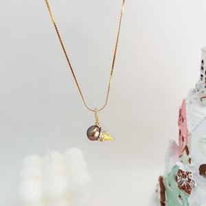 K&ouml;nnte beinhalten: Eine goldene Kettenkette mit einem Anh&auml;nger in Form eines goldenen Eisbechers mit einer dunkelbraunen Perle und kleinen klaren Steinen.