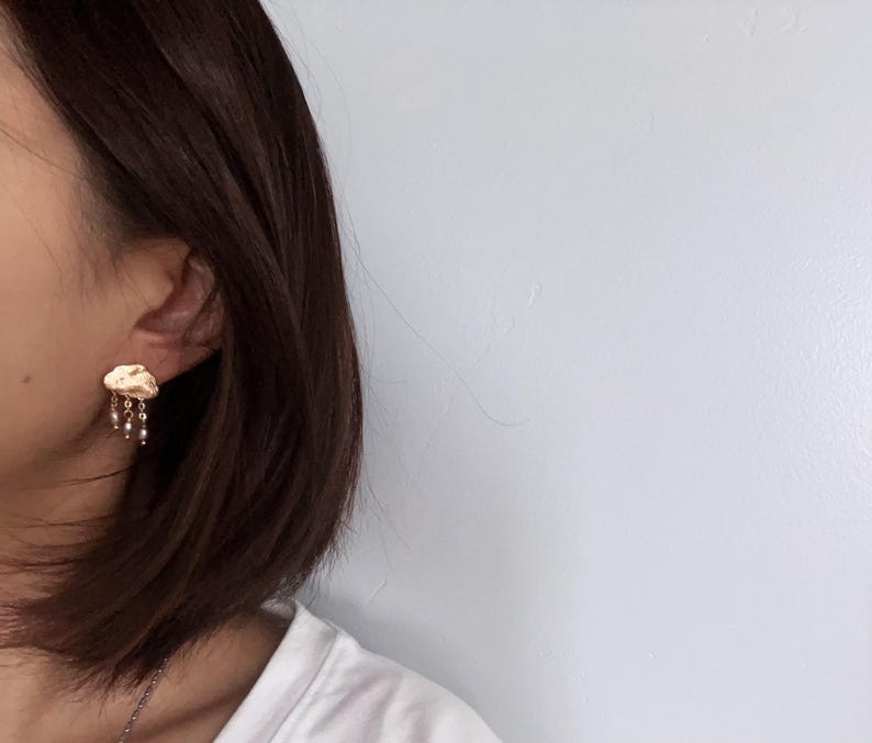 May include: Gold cloud-shaped earrings with a dangling chain of small pearls.