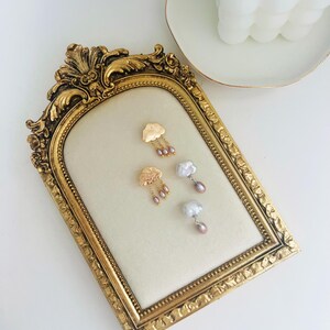 May include: Gold cloud earrings with pearl drops. The earrings are displayed on a gold ornate frame.