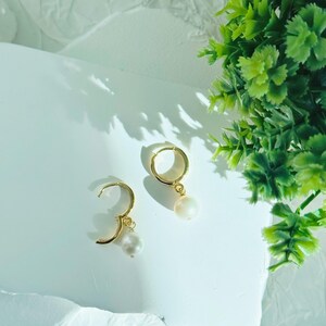 May include: A pair of gold hoop earrings with a single white pearl dangling from each hoop.
