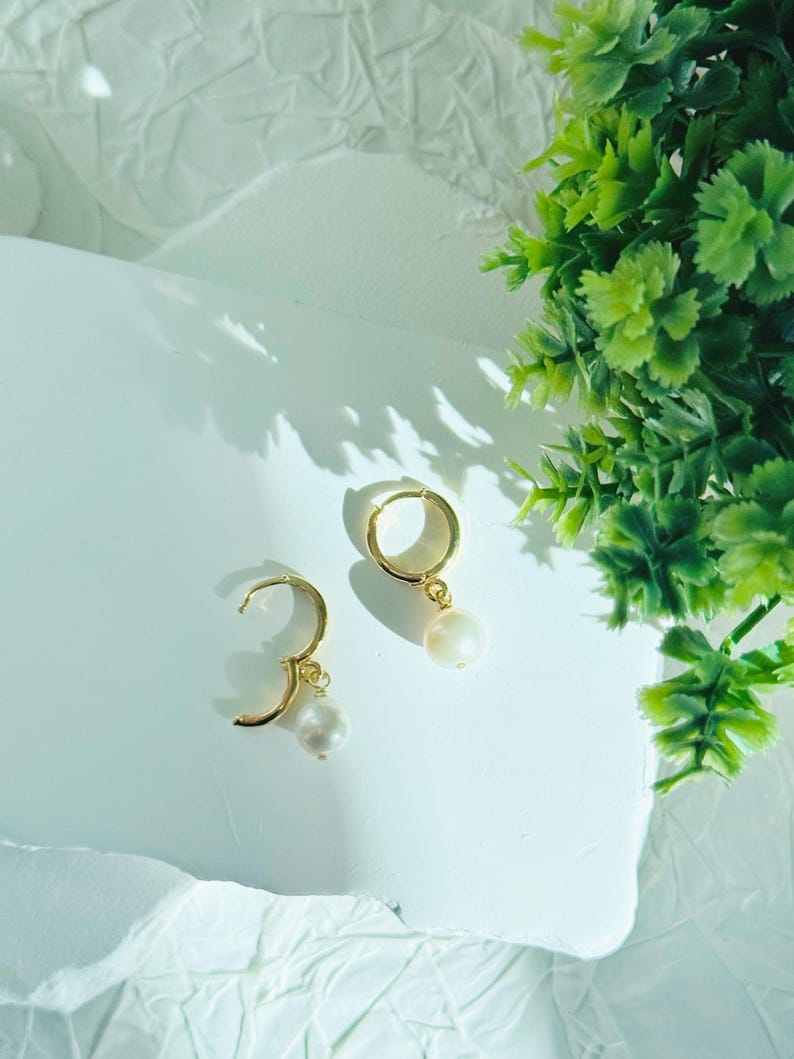 May include: A pair of gold hoop earrings with a single white pearl dangling from each hoop.