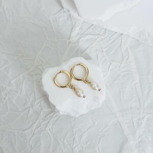 May include: A pair of gold hoop earrings with a single pearl dangling from each hoop.
