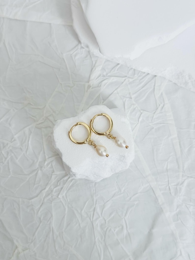 May include: A pair of gold hoop earrings with a single pearl dangling from each hoop.