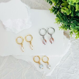 May include: Three pairs of hoop earrings with pearl drops. The earrings are in gold, silver, and rose gold. The pearls are white, pink, and gray.
