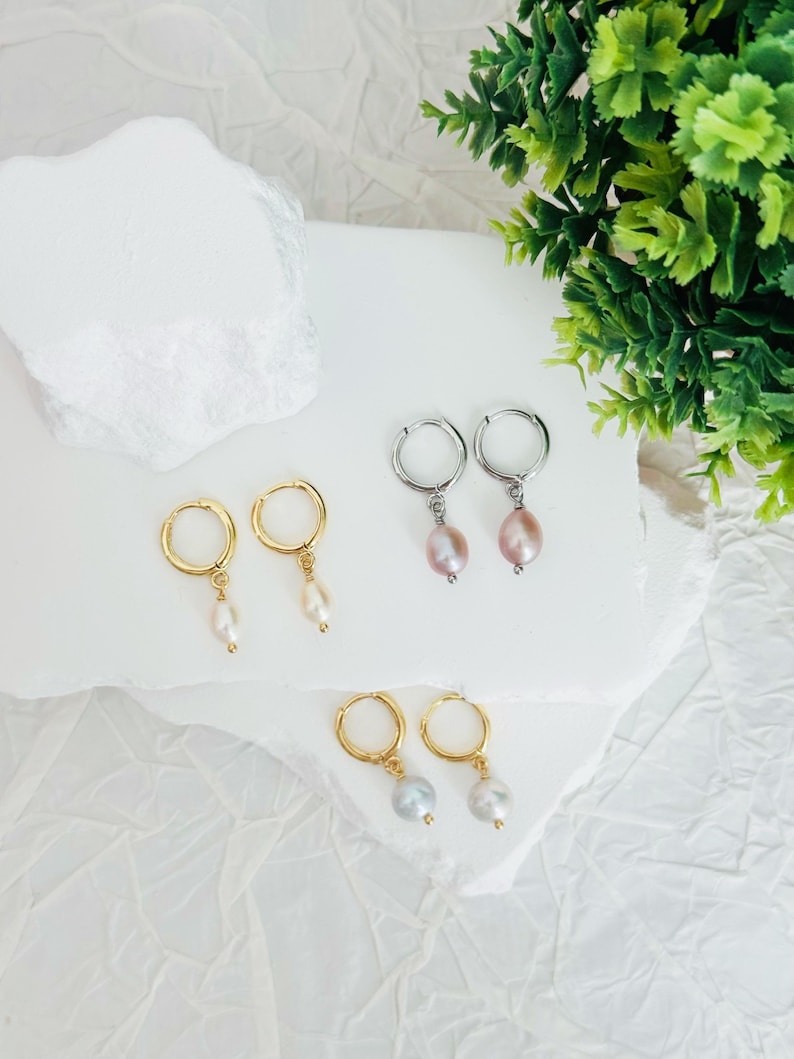 May include: Three pairs of hoop earrings with pearl drops. The earrings are in gold, silver, and rose gold. The pearls are white, pink, and gray.