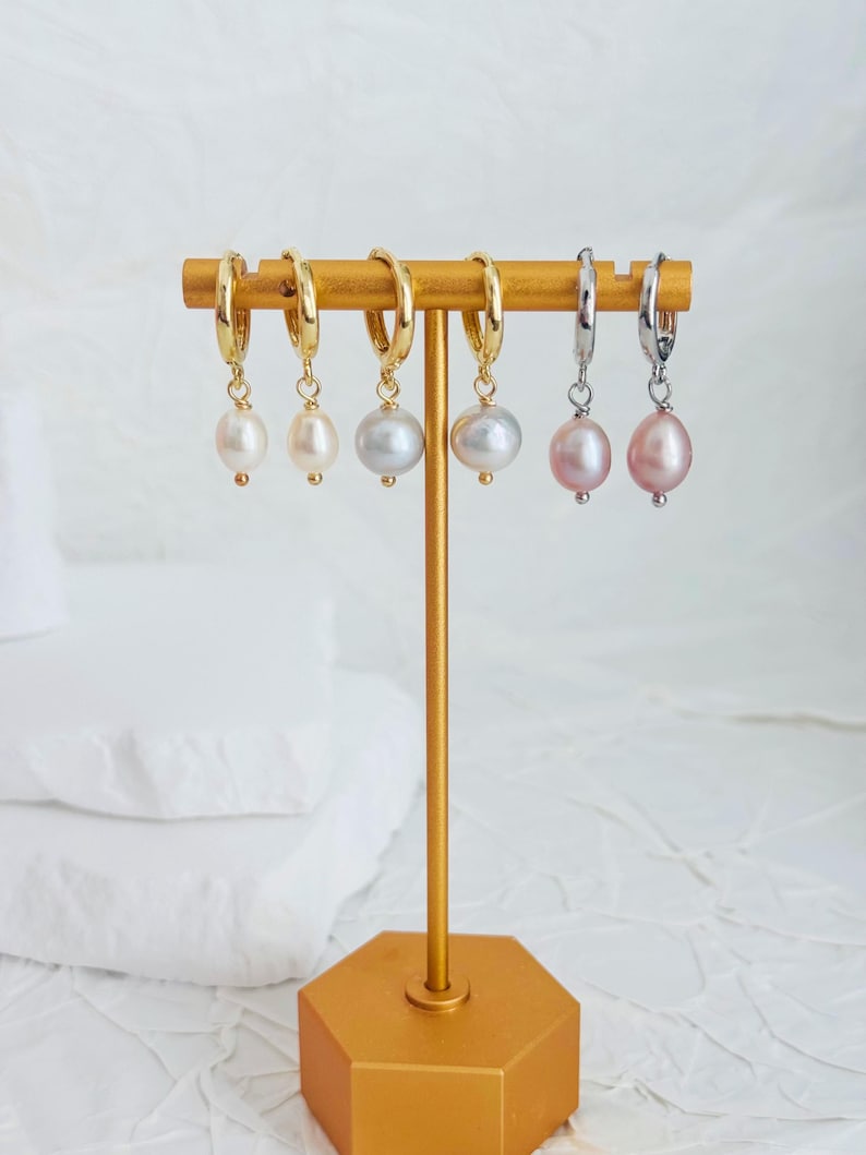 May include: Six pairs of hoop earrings with pearl drops. The hoops are gold and silver. The pearls are white and pink.
