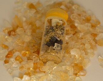 May include: A small glass bottle with a yellow lid filled with dried herbs, crystals, and gold glitter. The bottle is surrounded by small, clear and amber-coloured stones.