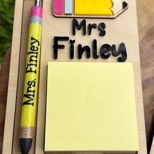 May include: Wooden desk organizer with a yellow pencil-shaped accent and a pen. The pen is yellow with glitter and the text "Mrs. Finley". Includes a yellow sticky note pad and the name "Mrs Finley" in black.