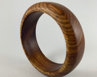 May include: A dark brown wooden bangle bracelet with a smooth, polished finish. The bracelet is made from a single piece of wood and has a natural grain pattern.
