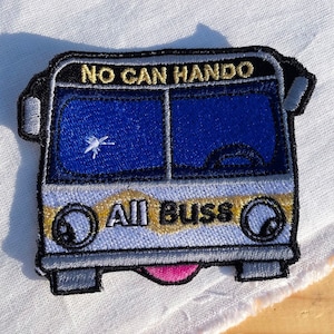 Puede incluir: Un parche bordado azul y blanco de un autobús con el texto "NO CAN HANDO" y "ALL BUSS" en la parte delantera. El autobús tiene una lengua rosa que sobresale.