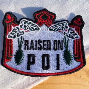 May include: A white embroidered patch with a red border and a crown at the top. The patch says "RAISED ON POI" with two green taro plants on either side.
