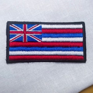 May include: An embroidered patch featuring the flag of Hawaii. The flag is red, white, and blue with a Union Jack in the upper left corner.