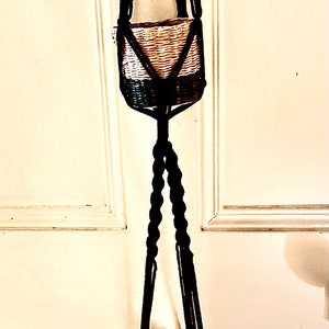 May include: Two black macrame plant hangers with woven baskets. The hangers are hanging from a white door.
