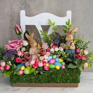 May include: A white wooden chair with a floral arrangement featuring pink and purple flowers, green leaves, and two bunny figurines. The arrangement is decorated with pastel-colored Easter eggs.