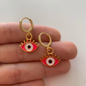 May include: A pair of gold hoop earrings with pink and white evil eye charms.
