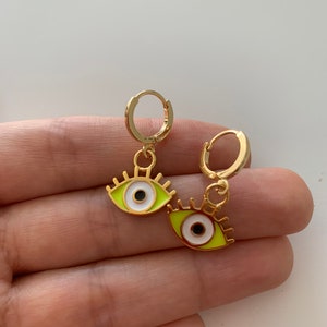 May include: A pair of gold hoop earrings with a green and white evil eye charm hanging from each hoop.