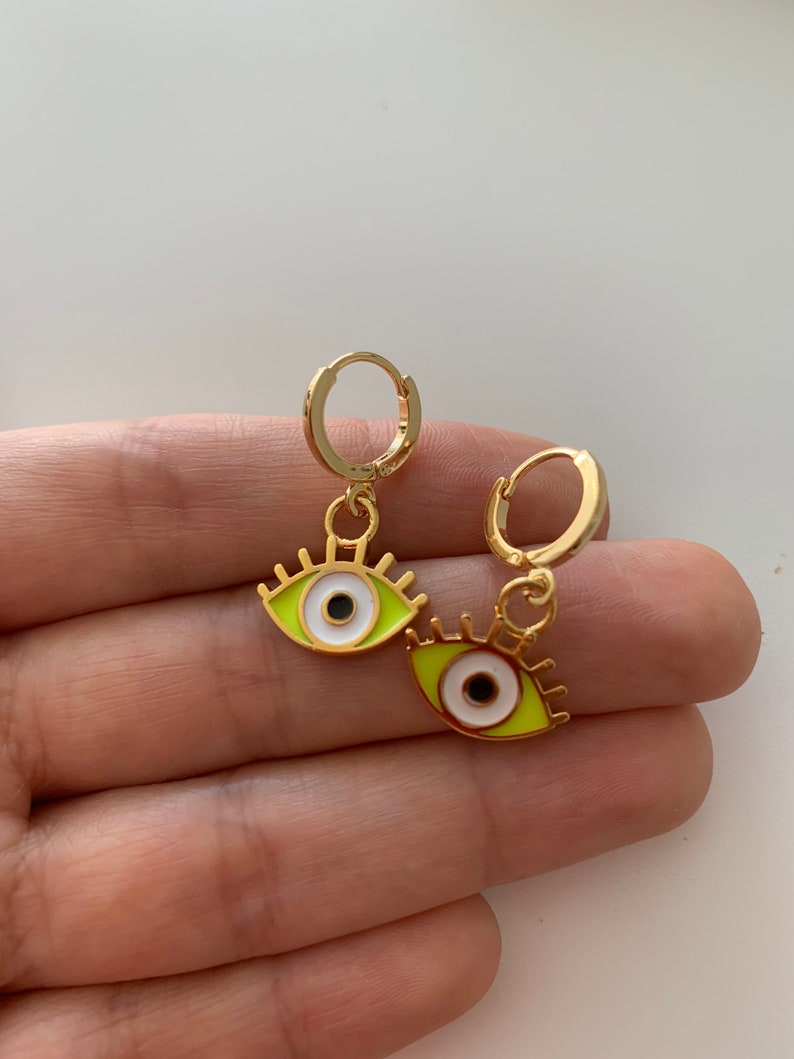 May include: A pair of gold hoop earrings with a green and white evil eye charm hanging from each hoop.