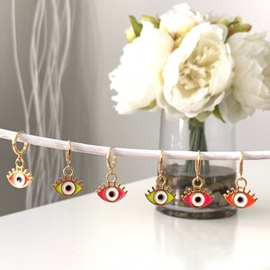 May include: Five gold hoop earrings with colorful eye charms. The eyes are outlined in gold and have white pupils. The colors of the eyes are red, green, yellow, and orange.