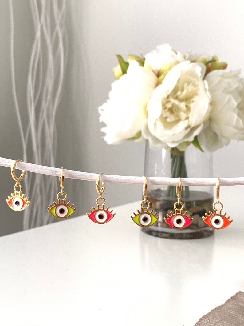 May include: Five gold hoop earrings with colorful eye charms. The eyes are outlined in gold and have white pupils. The colors of the eyes are red, green, yellow, and orange.