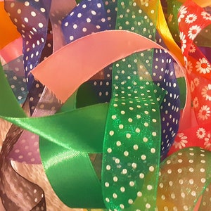 Op de afbeelding: Een kleurrijk assortiment linten in verschillende tinten, waaronder groen, roze, oranje en blauw. Sommige linten hebben stippen, andere bloempatronen. De linten zijn met elkaar verweven, waardoor een levendige en gestructureerde weergave ontstaat.