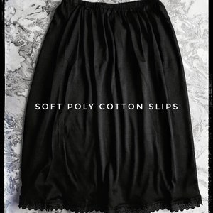 May include: A black slip skirt made from soft poly cotton. It features an elasticated waistband and a lace trim at the hem. The text "SOFT POLY COTTON SLIPS" is printed in white across the top of the skirt.