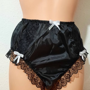 May include: Black satin underwear with lace trim and white satin bows. The underwear has a high-waisted design with a ruffled lace edge. The lace trim is black and the bows are white.