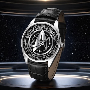Op de afbeelding: Een zilverkleurig analoog horloge met een zwarte lederen band met een textuurafwerking. De wijzerplaat is zwart en toont het zilveren Starfleet Command United Federation of Planets-logo, met zilveren wijzers en een zilverkleurige metalen kast.