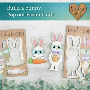 May include: Easter craft kit featuring bunny cutouts with glasses, carrots, and an Easter egg. The kit includes the text "Build a bunny. Pop out Easter Craft" and the "Restless Soul Designs" logo.