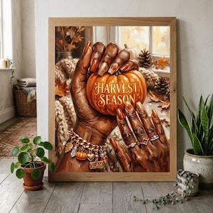 May include: A framed wall art print depicting dark-toned hands holding an orange pumpkin with the text HARVEST SEASON. The hands feature long, polished nails in shades of orange and gold, adorned with rings and a gold charm bracelet with pumpkin charms.