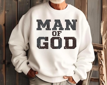 Op de afbeelding: Witte sweatshirt met de tekst "MAN OF GOD" in verweerde grijze letters. De sweatshirt heeft een ronde hals en lange mouwen. De afbeelding staat tegen een houten achtergrond.