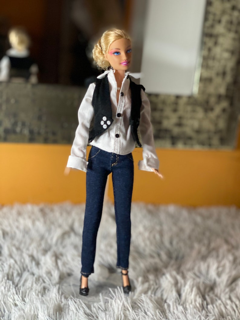 May include: A blonde doll wearing a white button-down shirt with a black vest, blue jeans, and black heels.