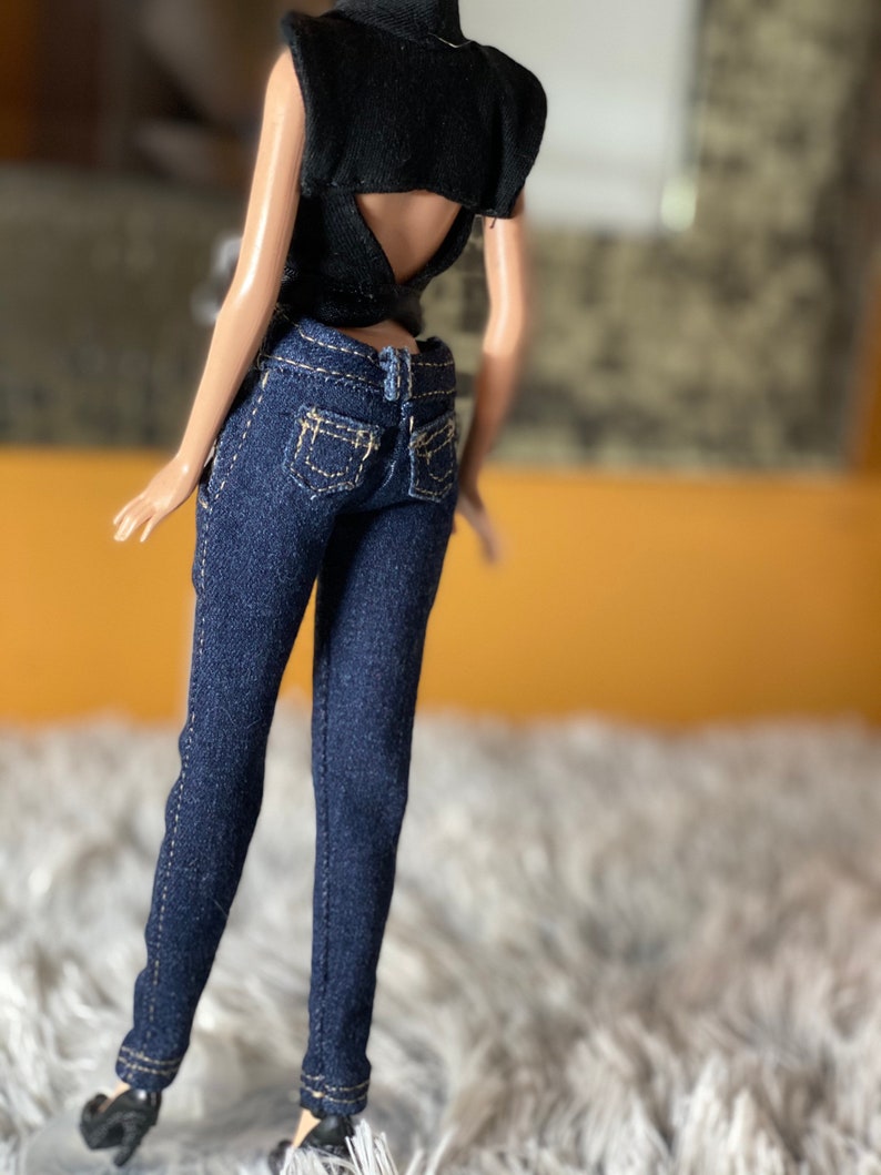 May include: A doll wearing a black sleeveless top with a low back and blue denim jeans.