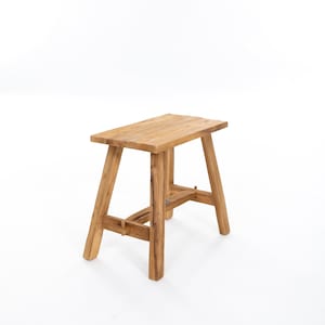 Op de afbeelding: Een houten kruk met een rechthoekig bovenblad en vier poten. De kruk is gemaakt van natuurlijk hout in een lichtbruine kleur.